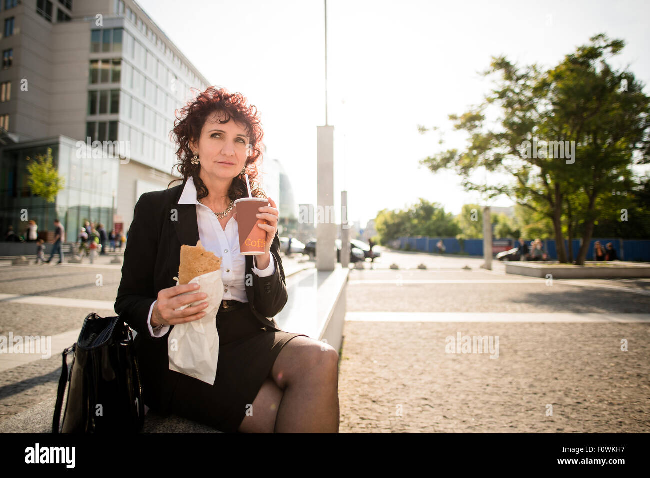 Mujer de negocios senior en comida rápida comida para llevar - beber café y comer sándwich en calle Foto de stock