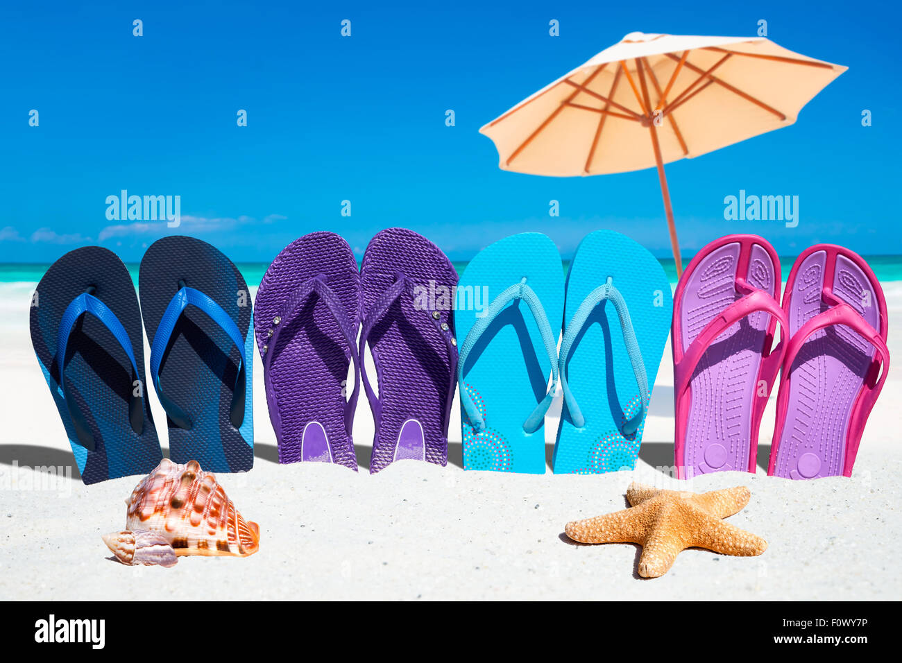 Algunos coloridos flip flops en una fila con estrellas de mar y concha en  primer plano y sombrillas en el fondo Fotografía de stock - Alamy