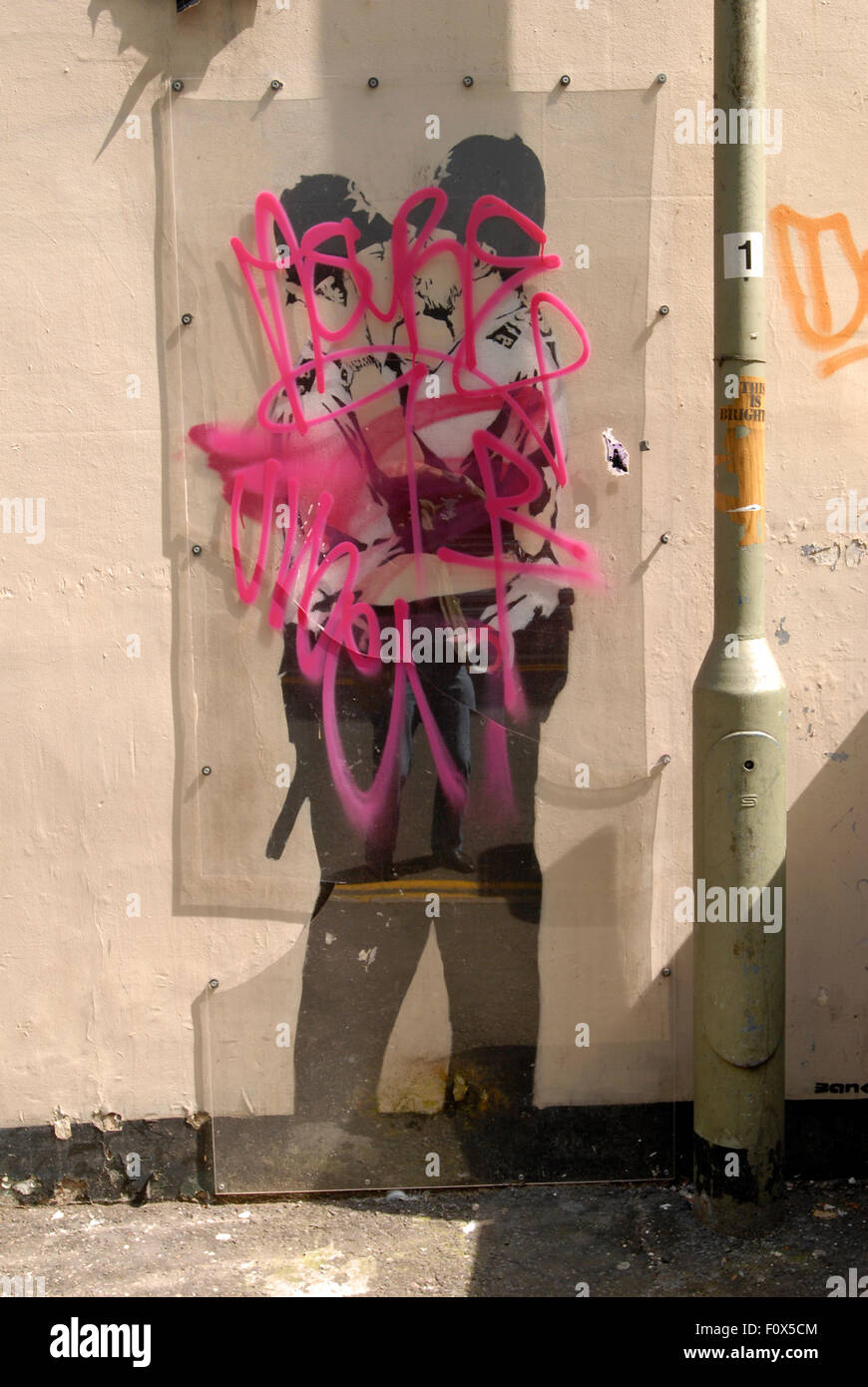 Etiquetas Graffiti rociados sobre la pantalla de plástico cubriendo el famoso Banksy besan Peroles de graffiti de dos besos gay policías en el lado del Prince Albert pub cerca de la estación de tren de Brighton. Foto de stock