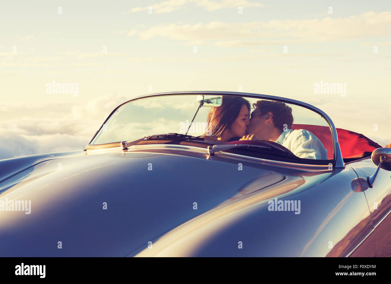 Romántica pareja atractiva joven contemplando el atardecer y besarse en Vintage clásico coche deportivo Foto de stock