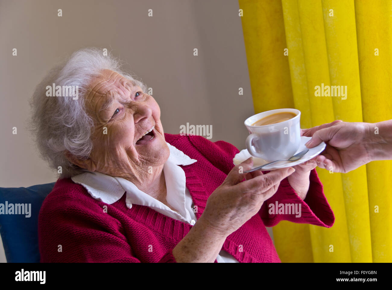 Los 90 ancianos cuidador cuidado té feliz visita al hogar feliz riendo anciana recibe una taza de té de cuidador enfermera acompañante en luz espacioso salón Foto de stock