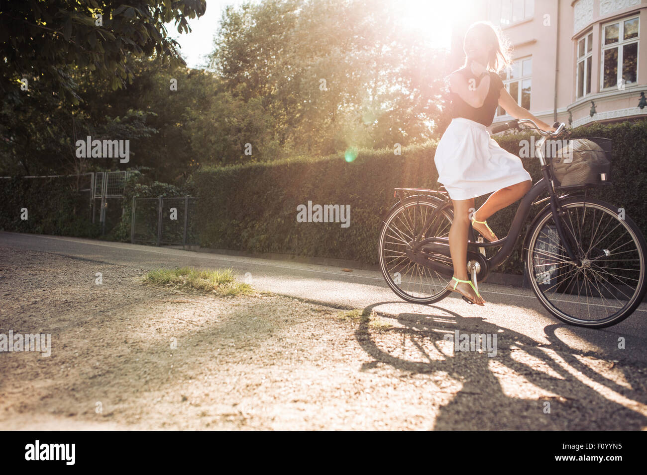 Disparó al aire libre de una joven mujer en bicicleta por la calle. Hembra con bicicleta Equitación llamarada solar. Foto de stock