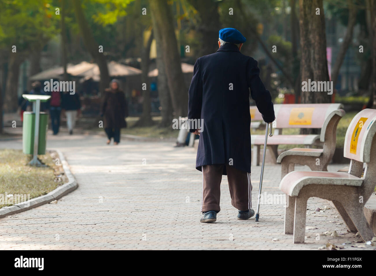 Hombre viejo caminando solo, vista trasera de un ciudadano mayor de Hanoi dando un paseo temprano por la mañana cerca del lago Hoan Kiem, Vietnam. Foto de stock