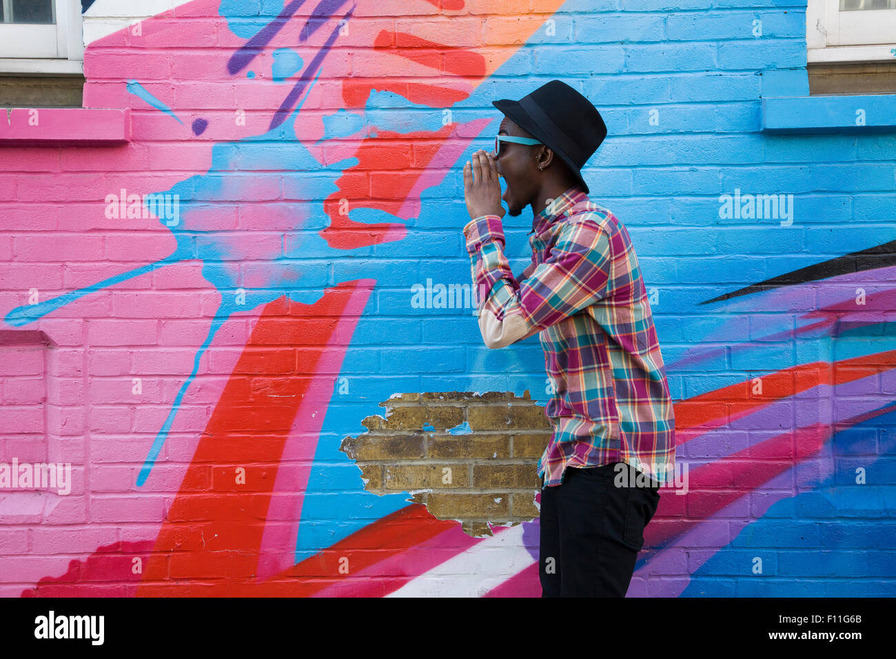 Hombre Negro en gafas de sol gritando cerca de paredes coloridas Foto de stock