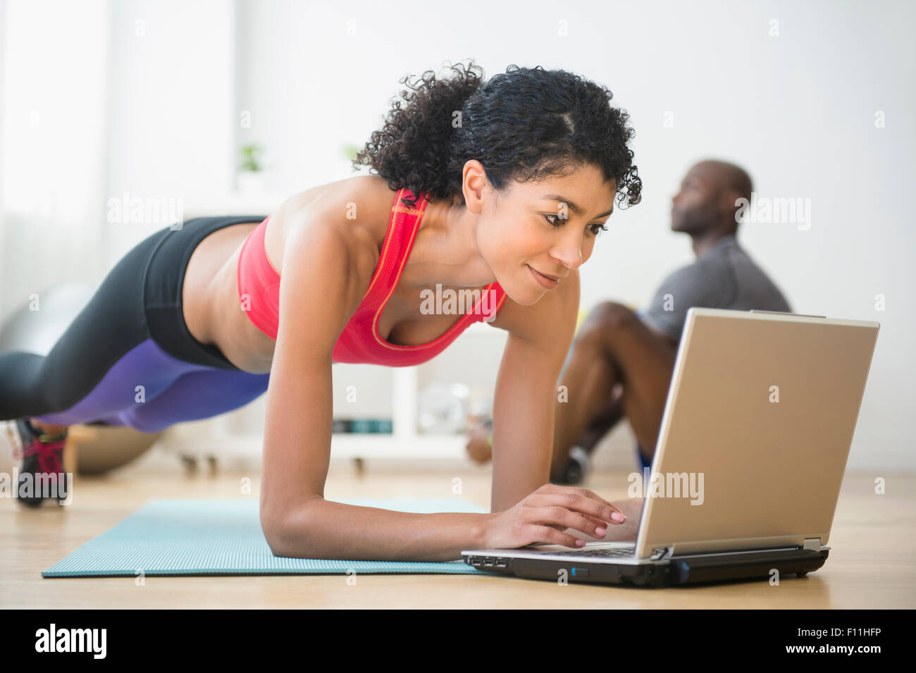 Mujer utilizando el ordenador y haciendo flexiones en el gimnasio Foto de stock