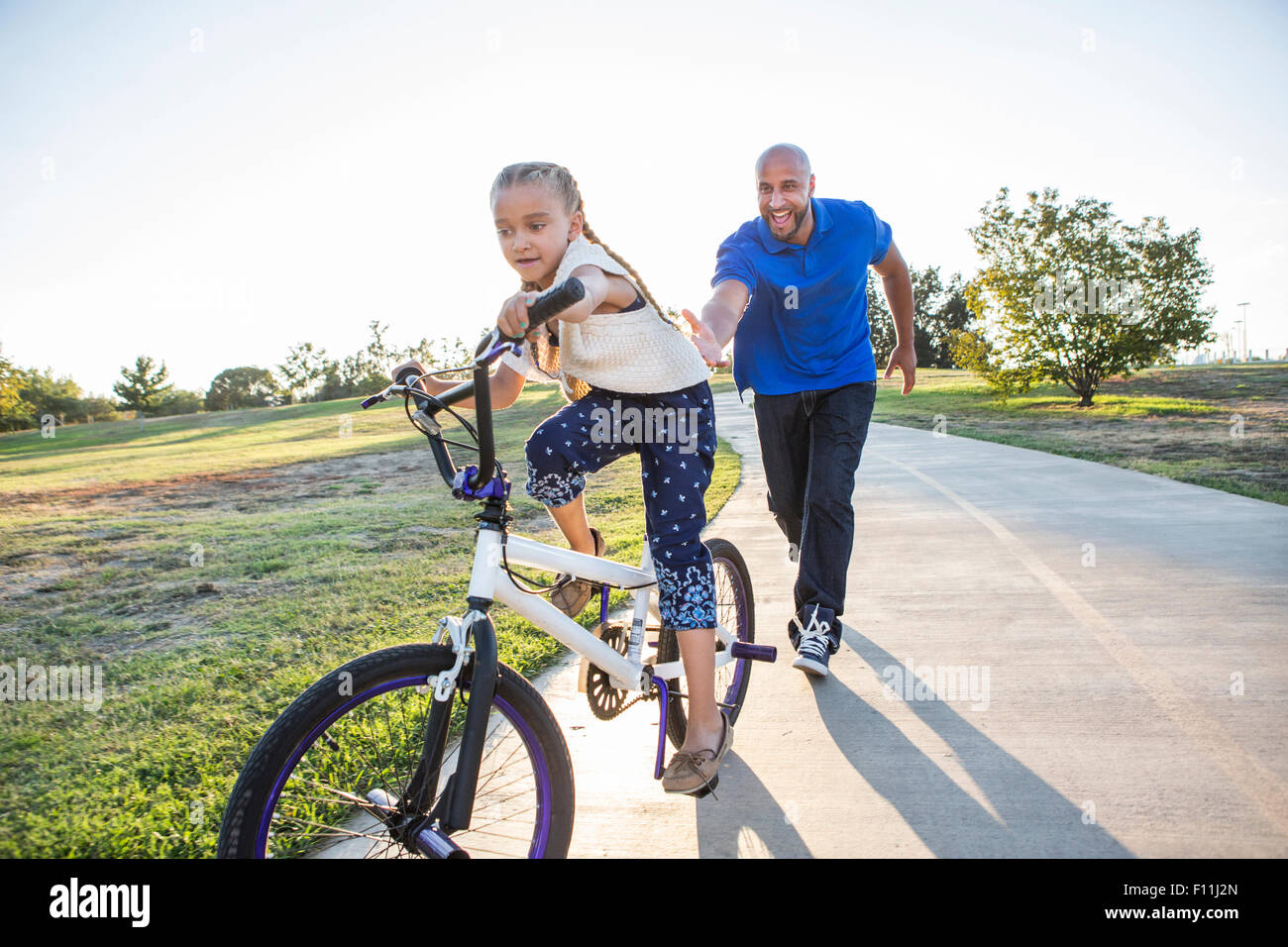 Hija de padre enseñar a andar en bicicleta en el parque Foto de stock