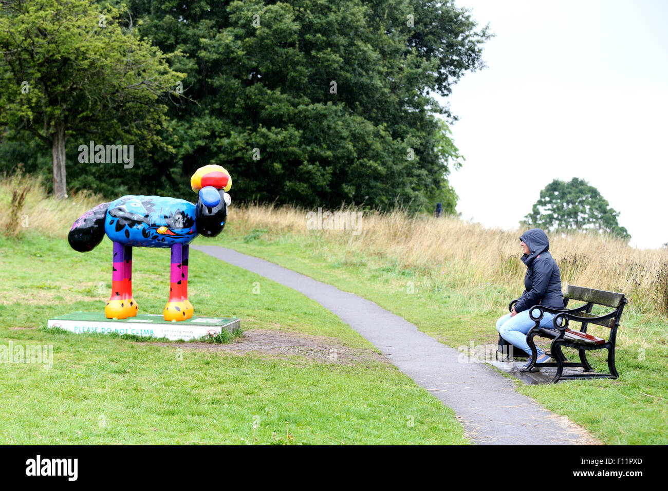 Sin inmutarse por la lluvia que un visitante se sienta a mirar un Shaun la oveja personaje. Parte del Bristol Shaun en la ciudad oveja trail 2015. Foto de stock