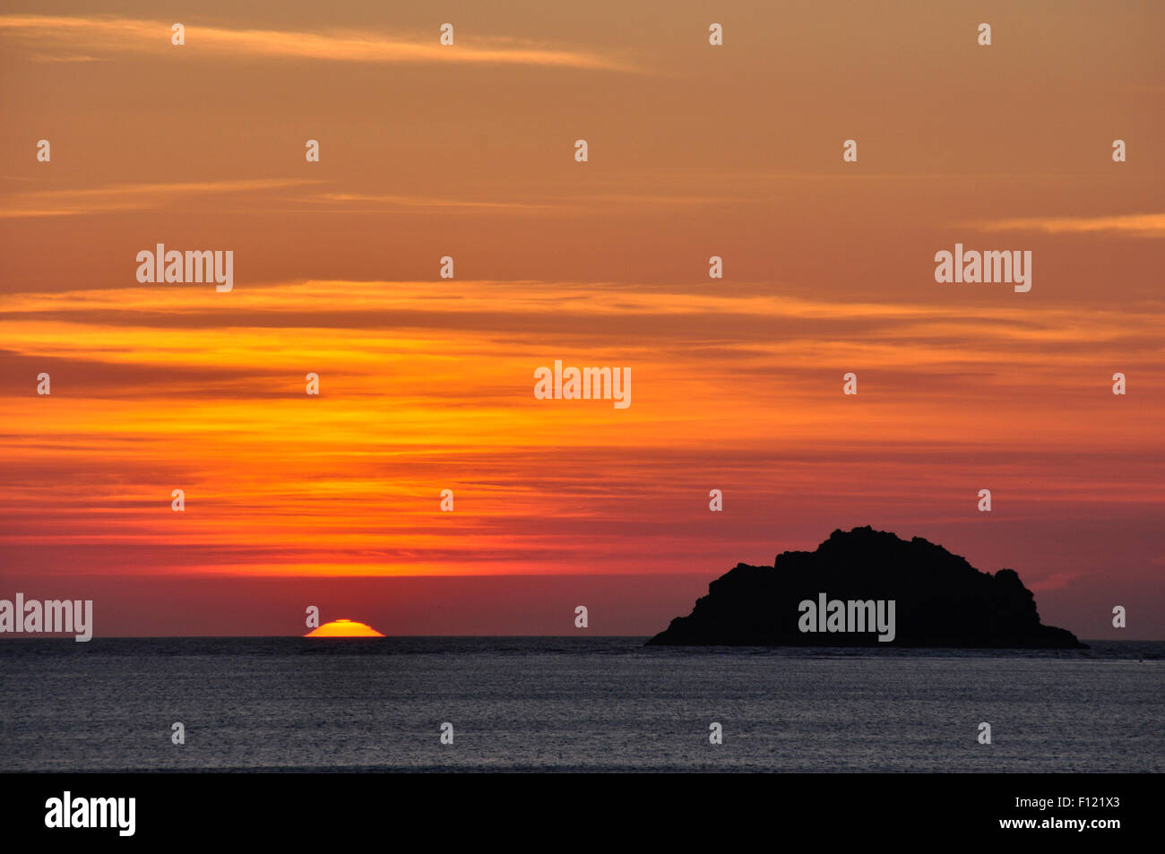 North Cornwall - puesta de sol tocando mar - isla en una silueta oscura - naranja - rojo y dorado moteadas cielo nuboso Foto de stock