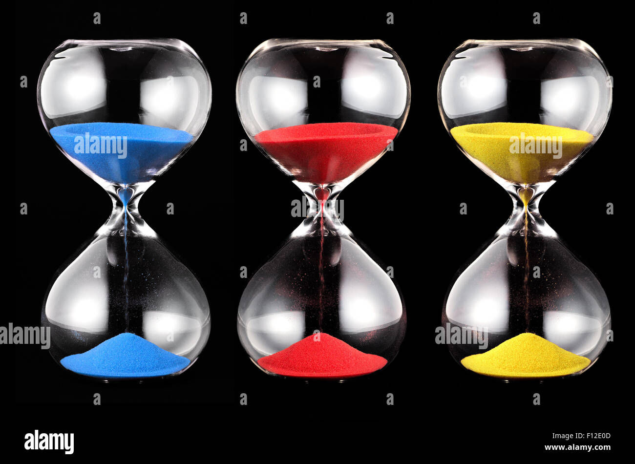 Tres relojes de arena con arena de colores, azul, rojo y amarillo, corriendo a través de las lámparas de cristal de medir el paso del tiempo Foto de stock