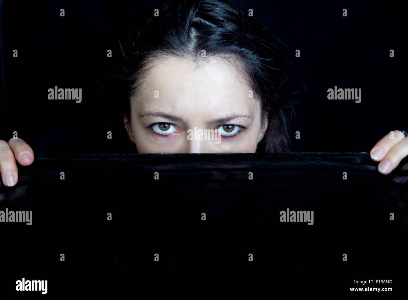 Mujer mirando con severidad desde detrás de un velo negro posee Foto de stock