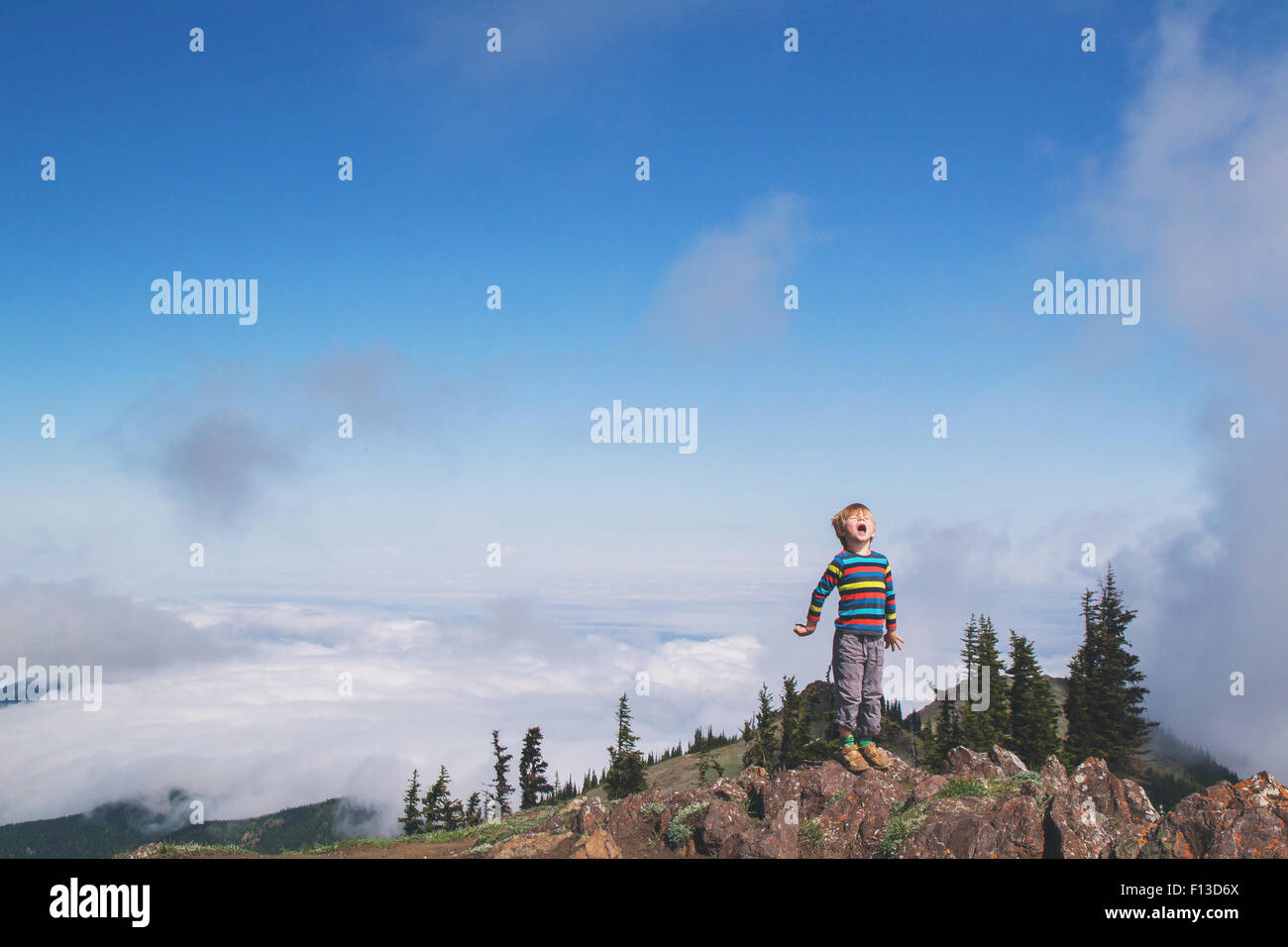 Niño de pie en la cima de una montaña gritar Foto de stock