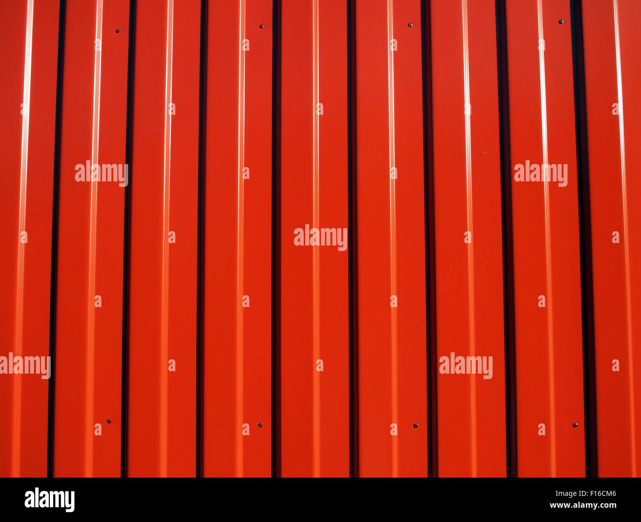 Metal rojo chapa ondulada con rayas longitudinales de rayas y sombras ilumina el sol brillante para utilizar como fondo Foto de stock