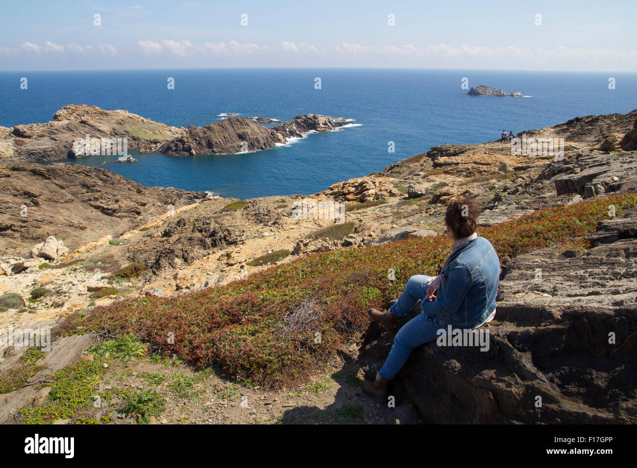 Mujer joven mirando hacia el mar, sentada en una roca Foto de stock