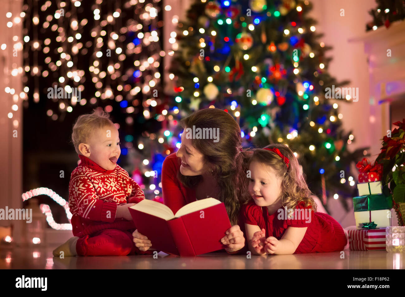 Hijo da un regalo de Navidad para mamá. Mamá agradablemente sorprendido y  lindo mira al niño. Aislado en un árbol de Año Nuevo fondo con regalos, un  fireplac Fotografía de stock 