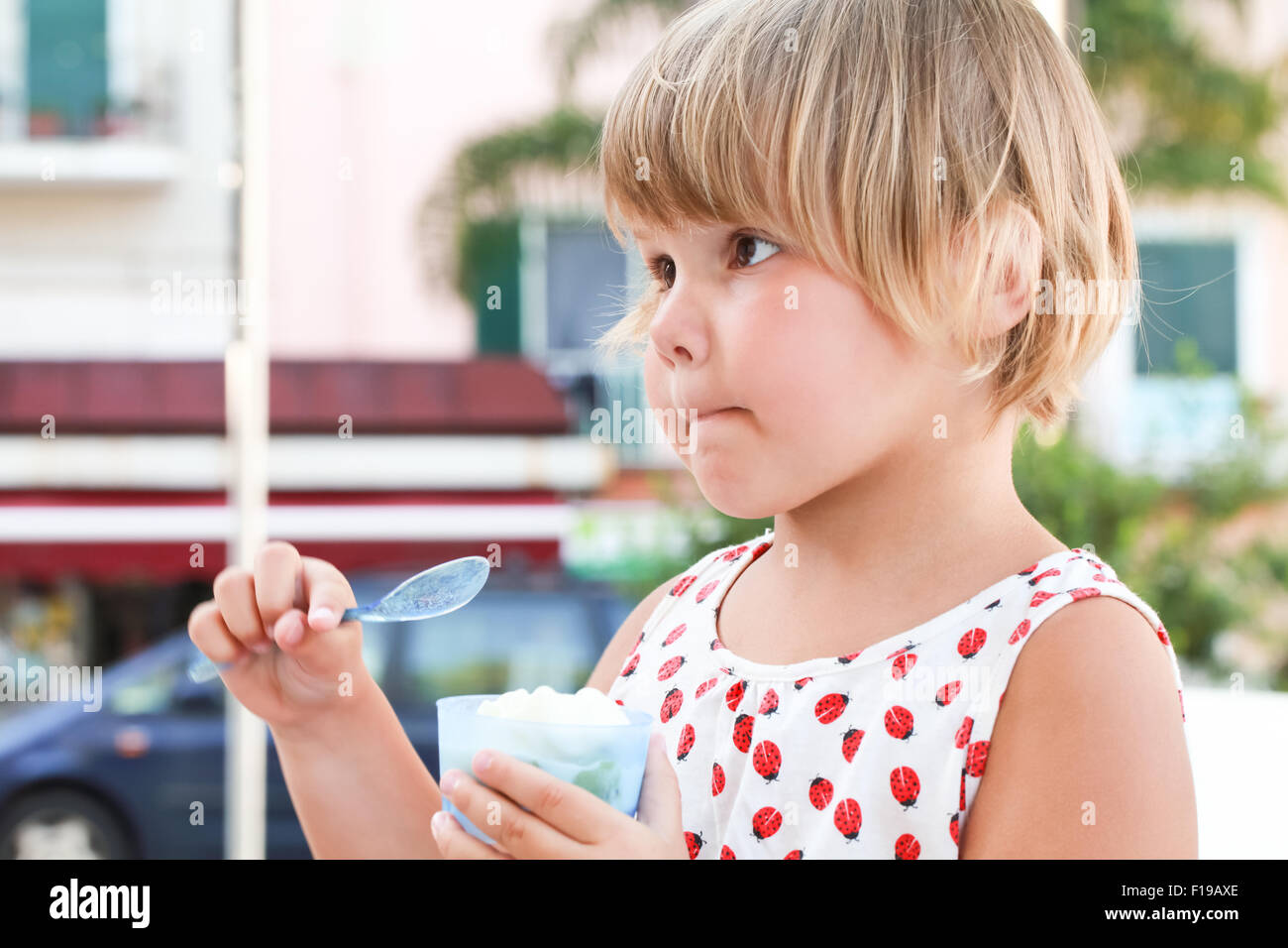 Niña caucásica rubia come helado de yogur, closeup retrato en exteriores con luz natural Foto de stock