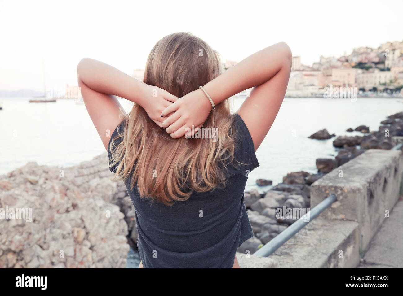 Caucásica rubia adolescente de pie sobre un mar tima, vista posterior, Gaeta, Italia Foto de stock