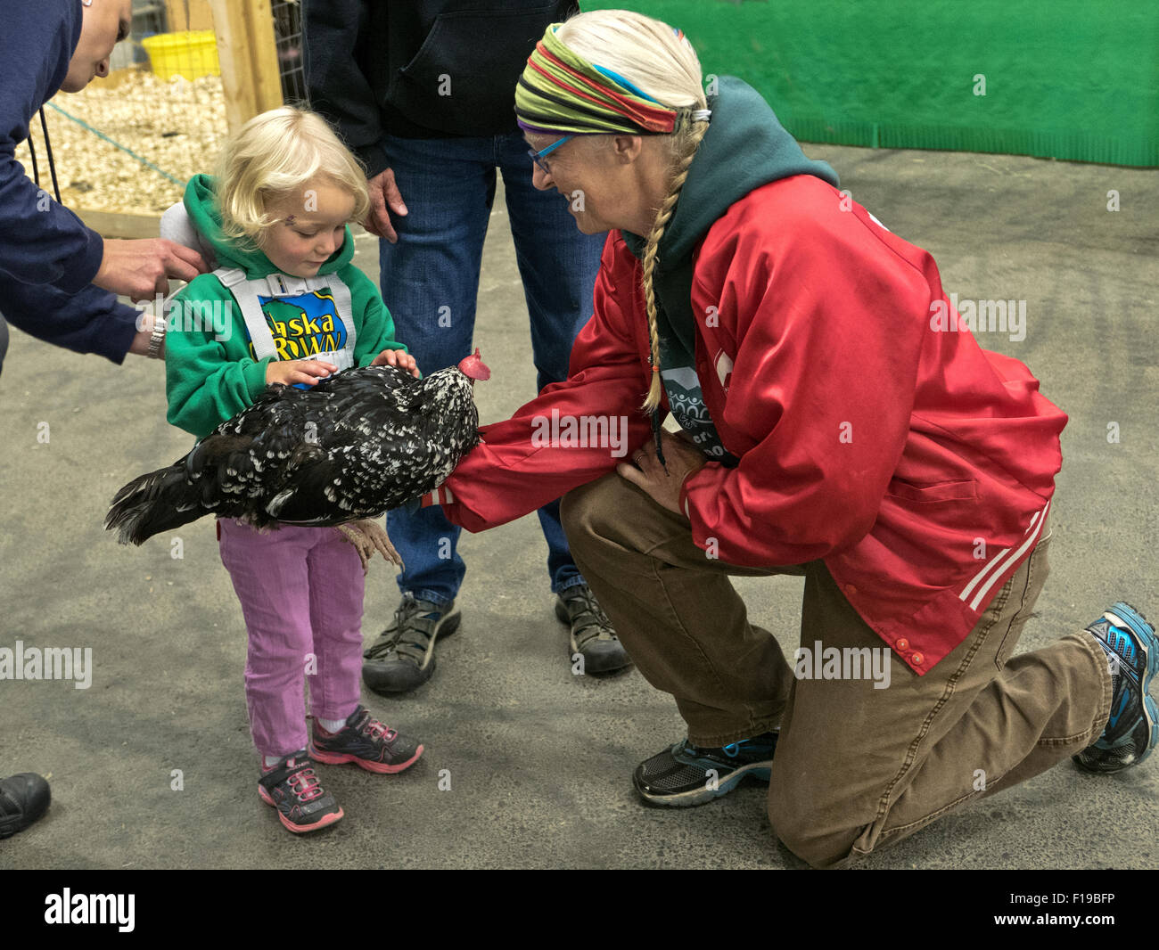 Granjero sosteniendo pollo domesticado, explicando a la joven admirando a la niña, la Feria del Estado de Alaska. Foto de stock