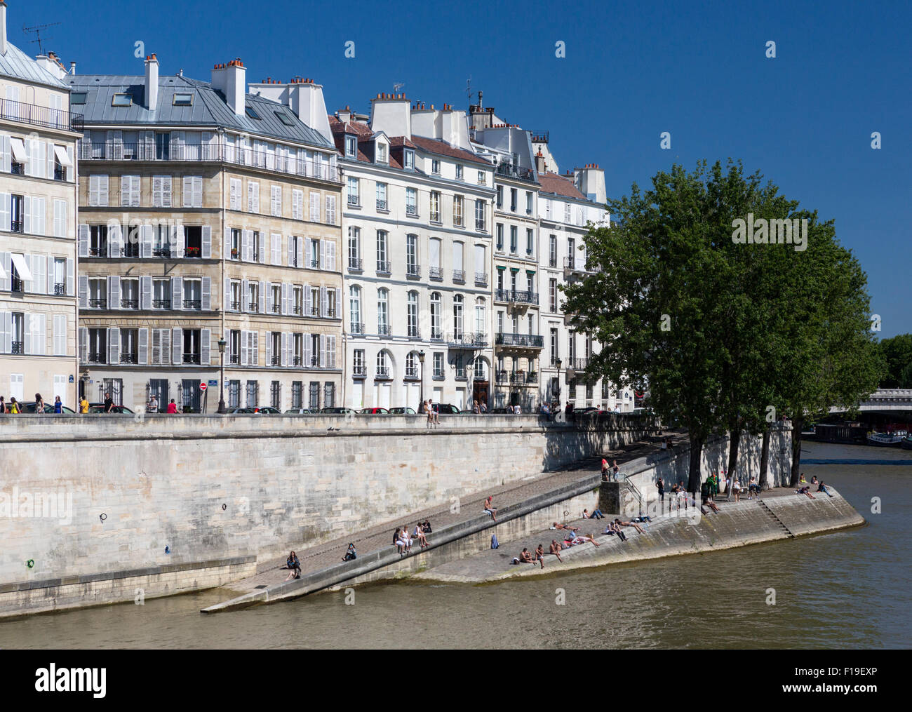 La primavera en París: Quai d'Orleans & Ile St Louis con los parisinos tomando sol en el muelle cerca del río Sena. Foto de stock