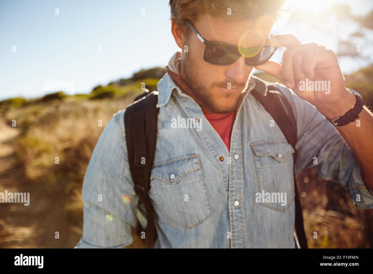 Primer plano de joven el país caminata. Modelo masculino caucásico senderismo con gafas de sol con la llamarada solar. Foto de stock