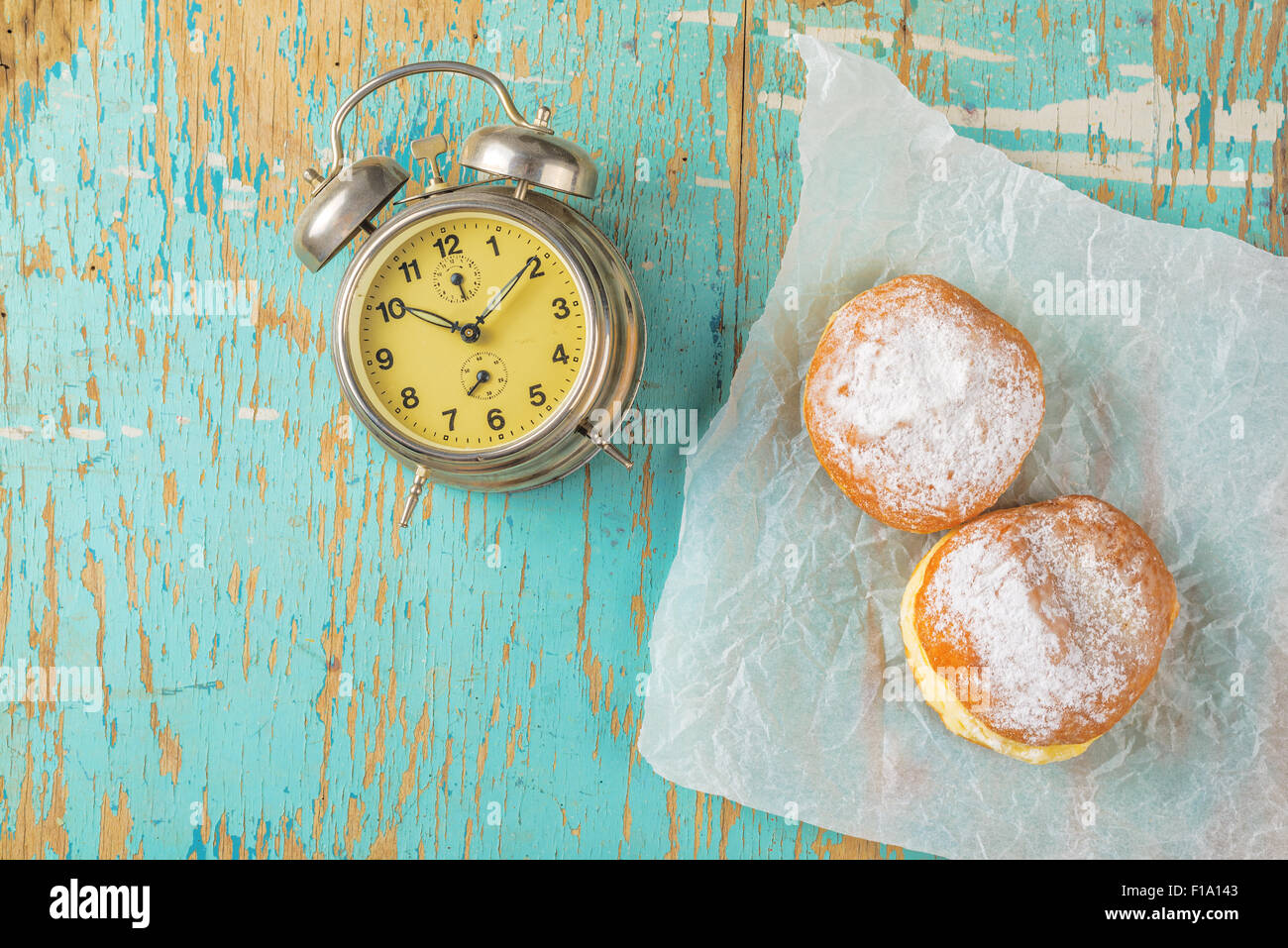 Dulces donas azucaradas y vintage despertador sobre la mesa de la cocina de madera rústica, vista superior de sabrosos buñuelos de panadería en vintage retro Foto de stock