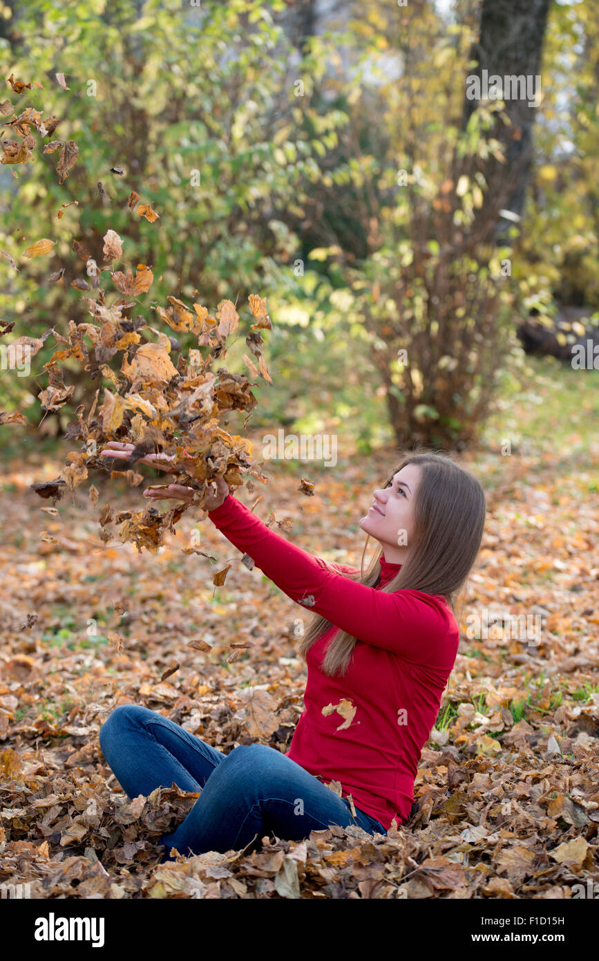 Feliz niña jugando con el otoño hojas amarillas en estacionamiento Foto de stock