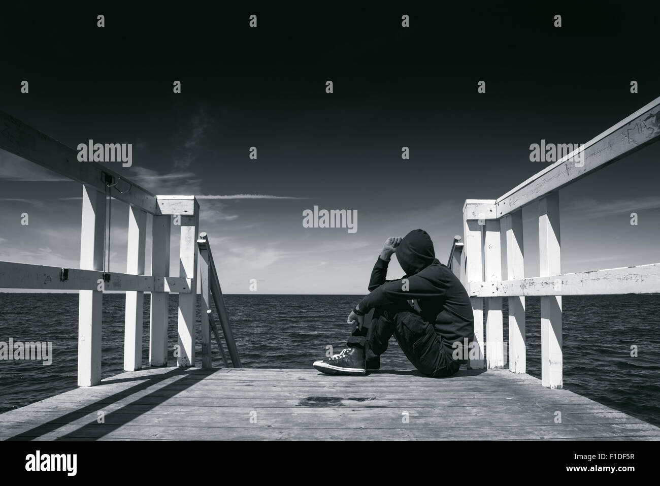 Solo hombre sentado en el borde del muelle de madera, mirando el agua - la desesperanza, la soledad, la alienación concepto, en blanco y negro Foto de stock