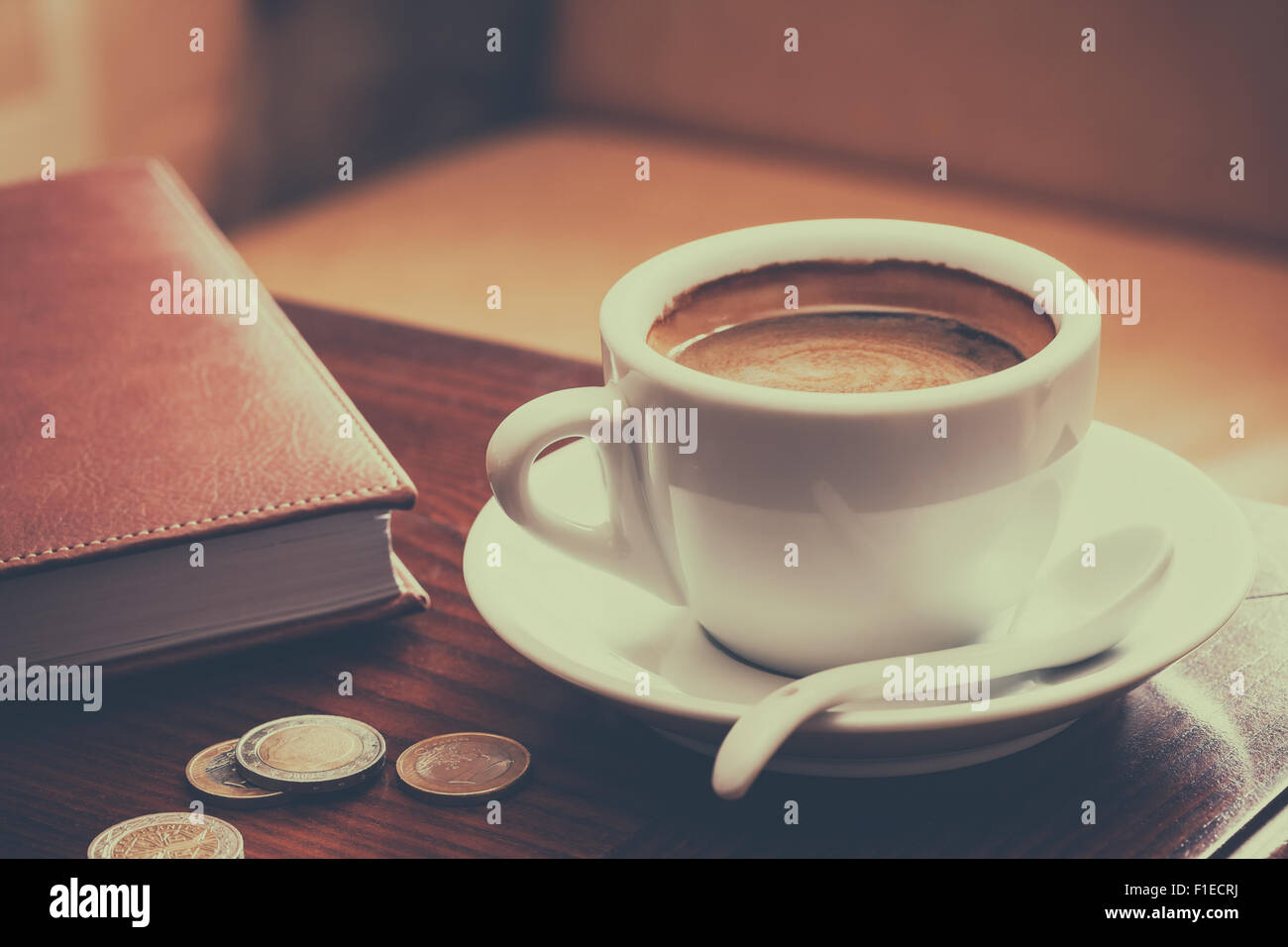 Vintage foto estilizada de la taza de café, diario y monedas sobre la mesa del café Foto de stock