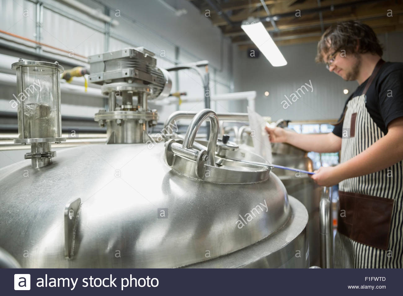 Trabajador con portapapeles en tanque de fermentación en destilería Foto de stock
