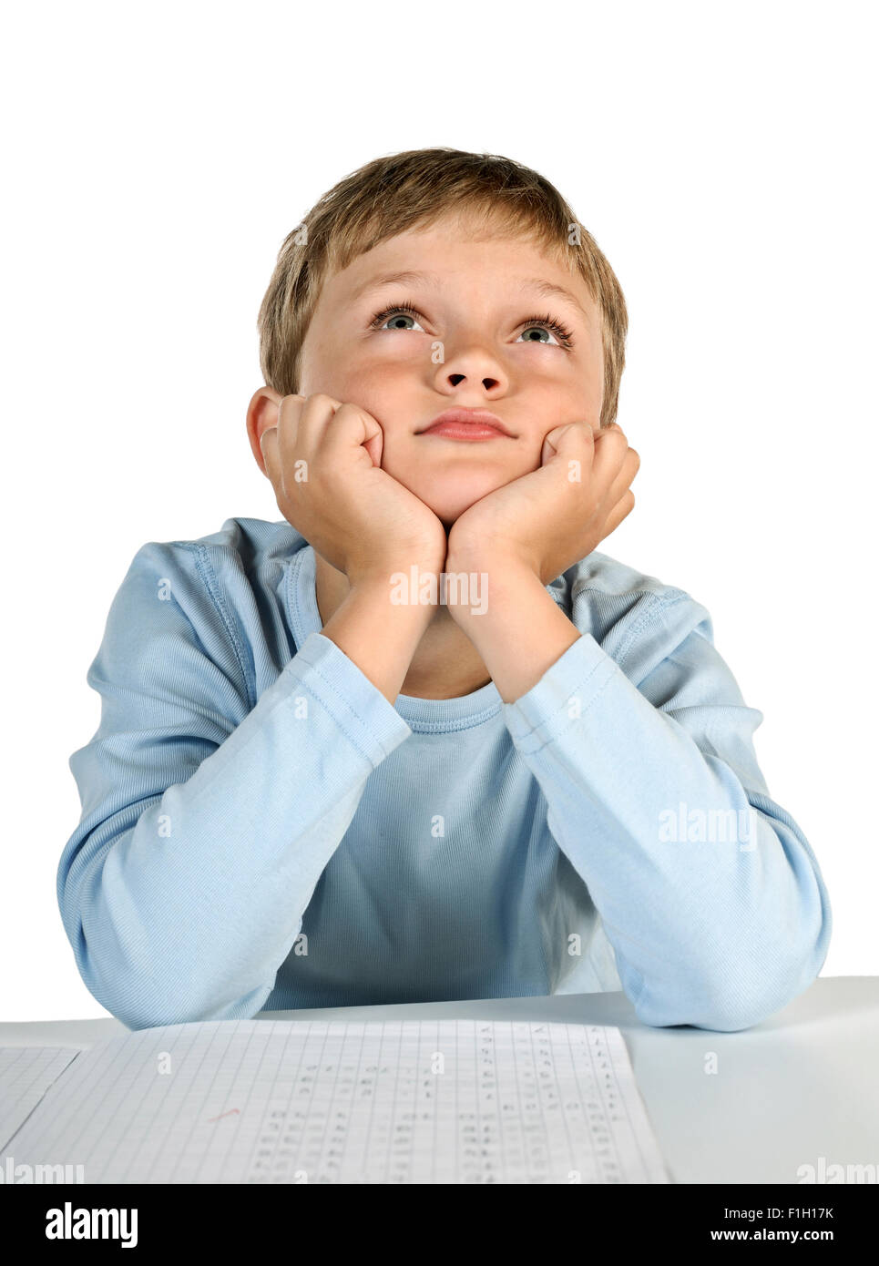 Niño sentado a la mesa, apoyando su cabeza en sus manos y los sueños. Foto de stock