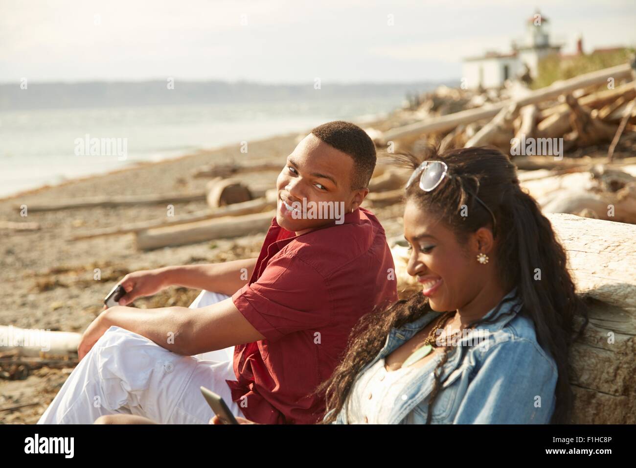 Pareja joven sentados juntos en la playa sonriente Foto de stock