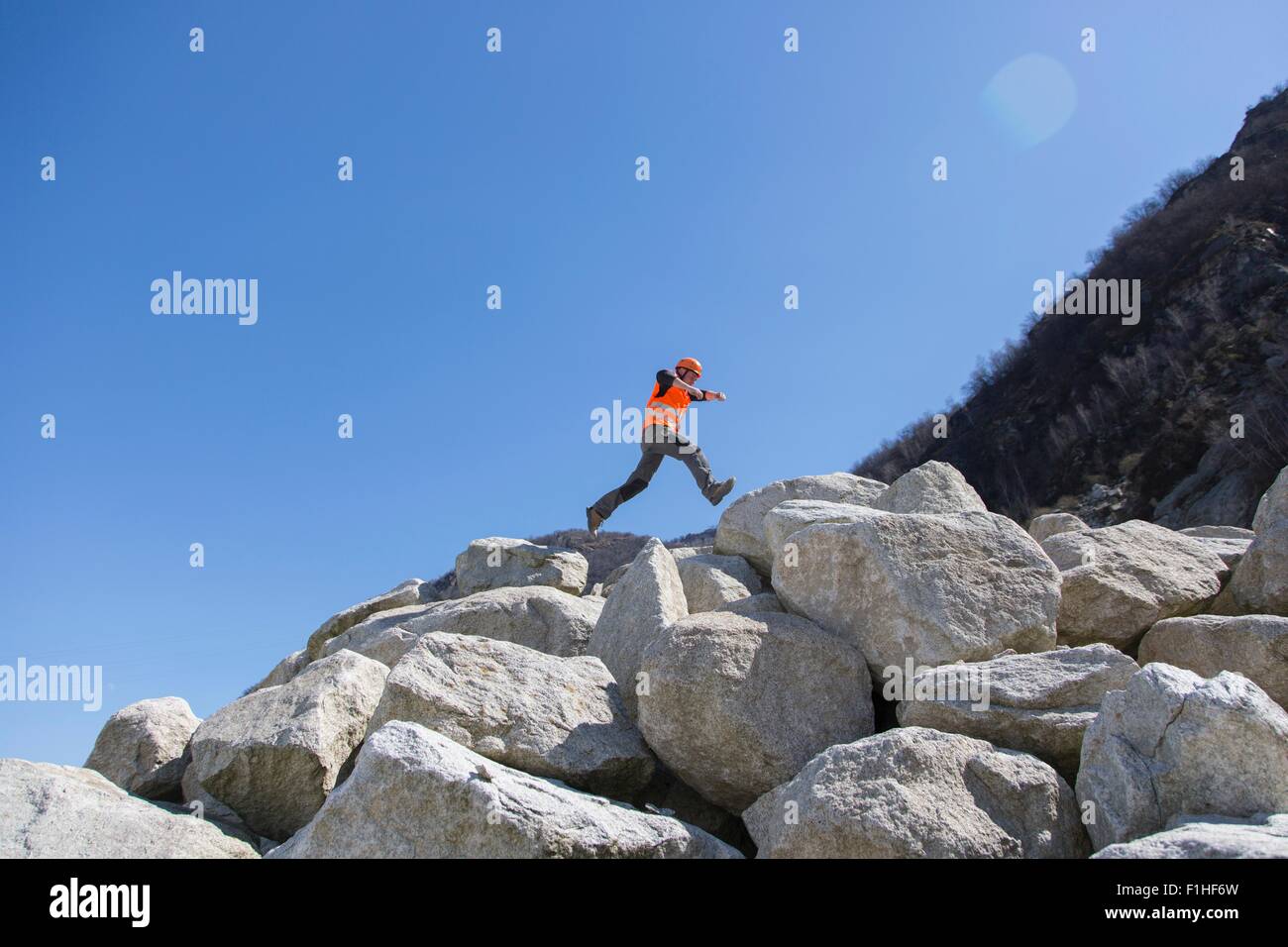 Trabajador saltando sobre una pila de rocas en cantera Foto de stock