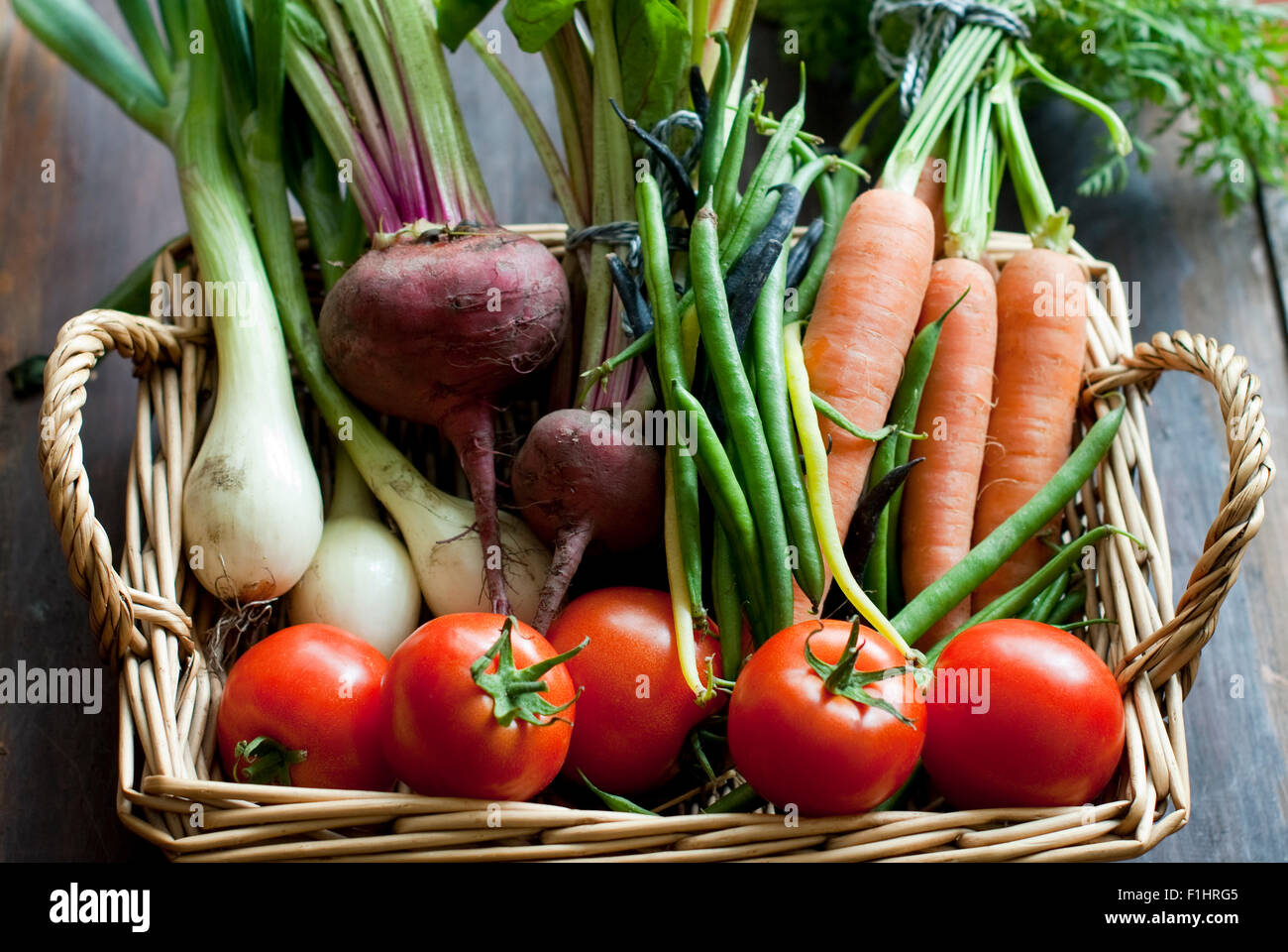 Verduras de verano orgánicos incluyendo tomates, frijoles, remolacha, cebolla y zanahorias con frondosos tops en una cesta de mimbre. Foto de stock