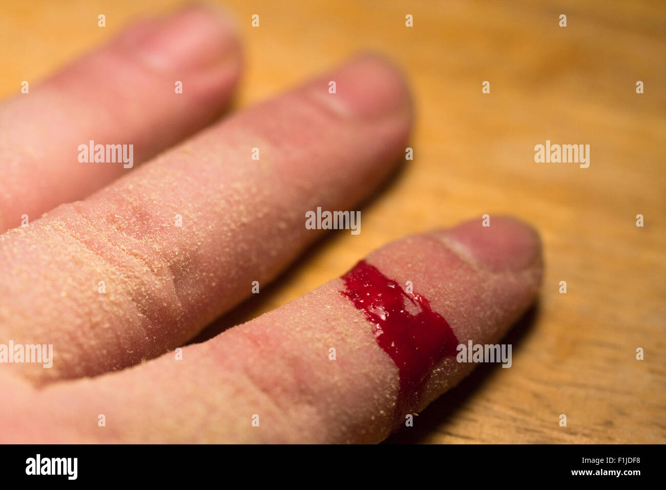 Un hombre del dedo índice cubierto con aserrín, mientras que la sangre fluye de una herida abierta sobre la mesa de madera Foto de stock
