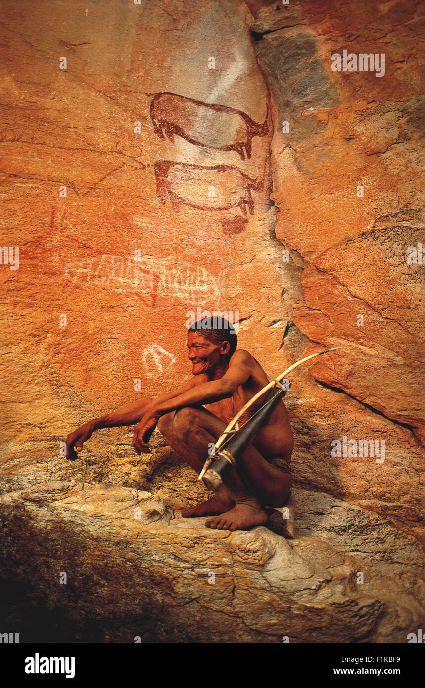 Bushman en cuclillas delante de pinturas rupestres con arco y flecha. Botswana, África Foto de stock