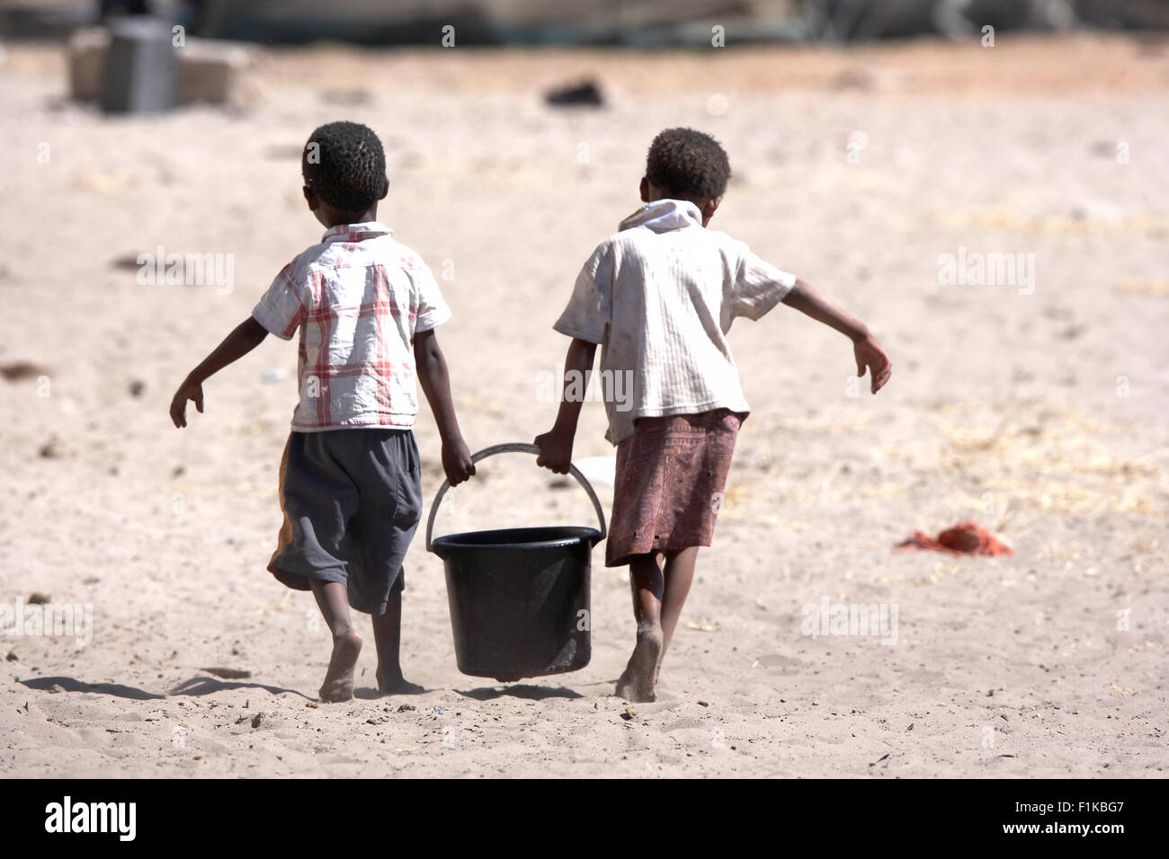 Dos niños bushman llevando un balde de agua, Xai Xai, Botswana Foto de stock