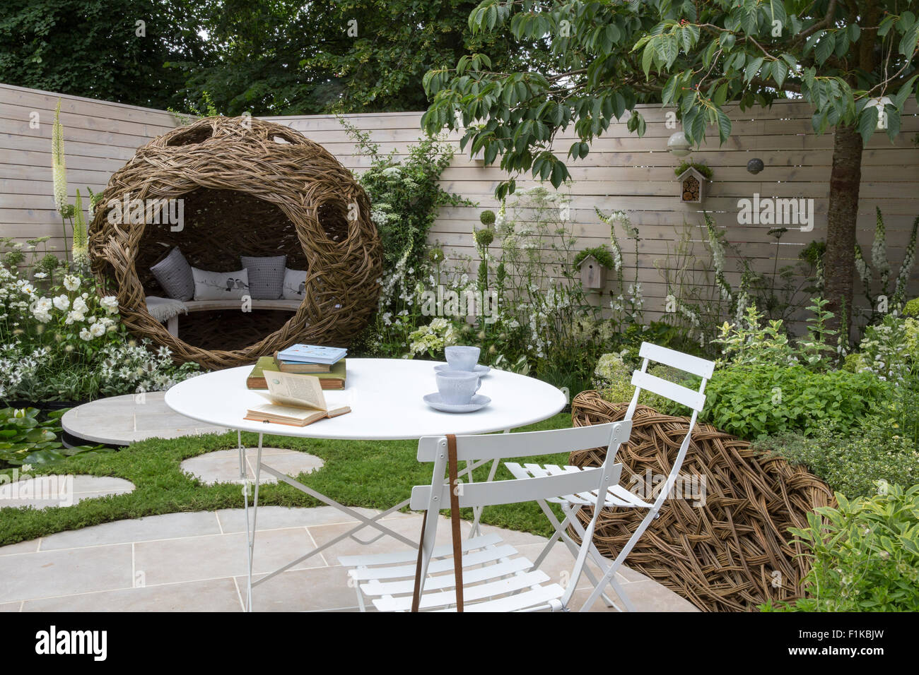 Pequeño espacio de jardín urbano redondo círculo de piedra sillas de mesa de patio circular valla pintada césped de manzanilla piedras de escalonamiento flores blancas en las fronteras del Reino Unido Foto de stock