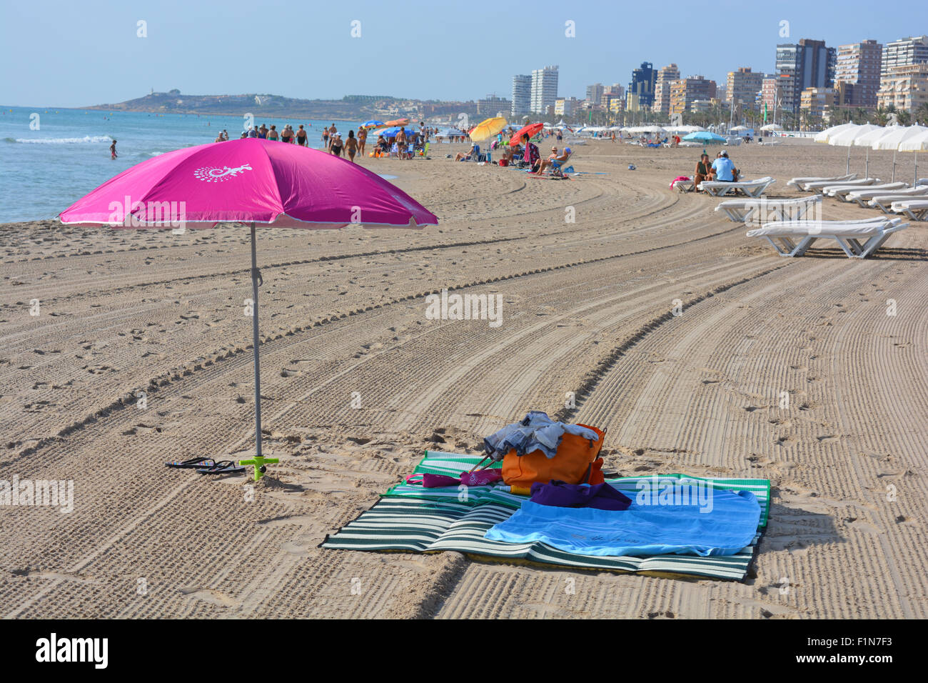 La sombrilla y toallas de playa en la playa de Campello, mirando hacia la ciudad de Alicante en la Costa Blanca, España Foto de stock