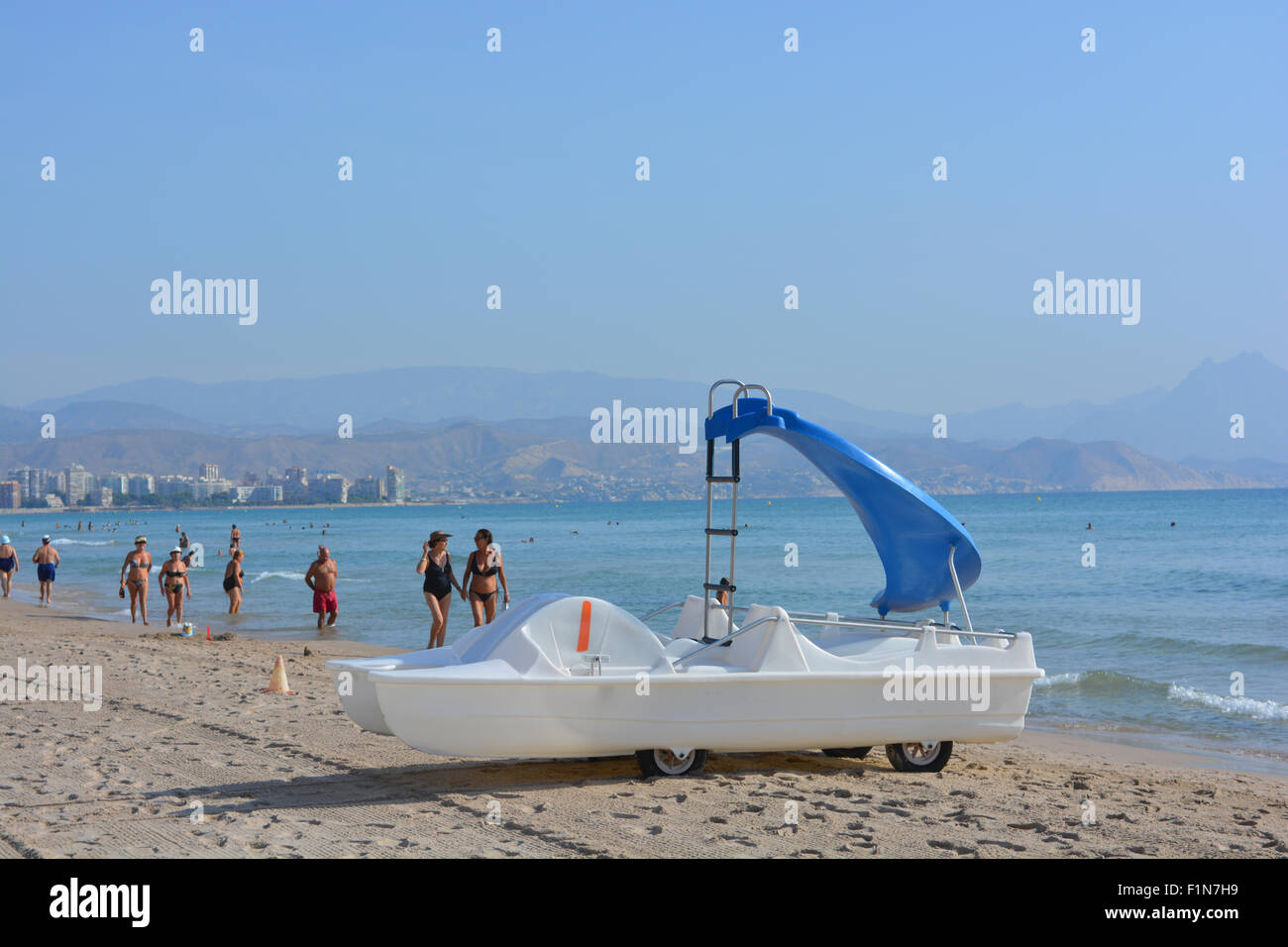 Un hidropedal barco con tobogán de agua para alquilar en la playa de Campello, temprano en la mañana con senderistas, Alicante, España. Foto de stock