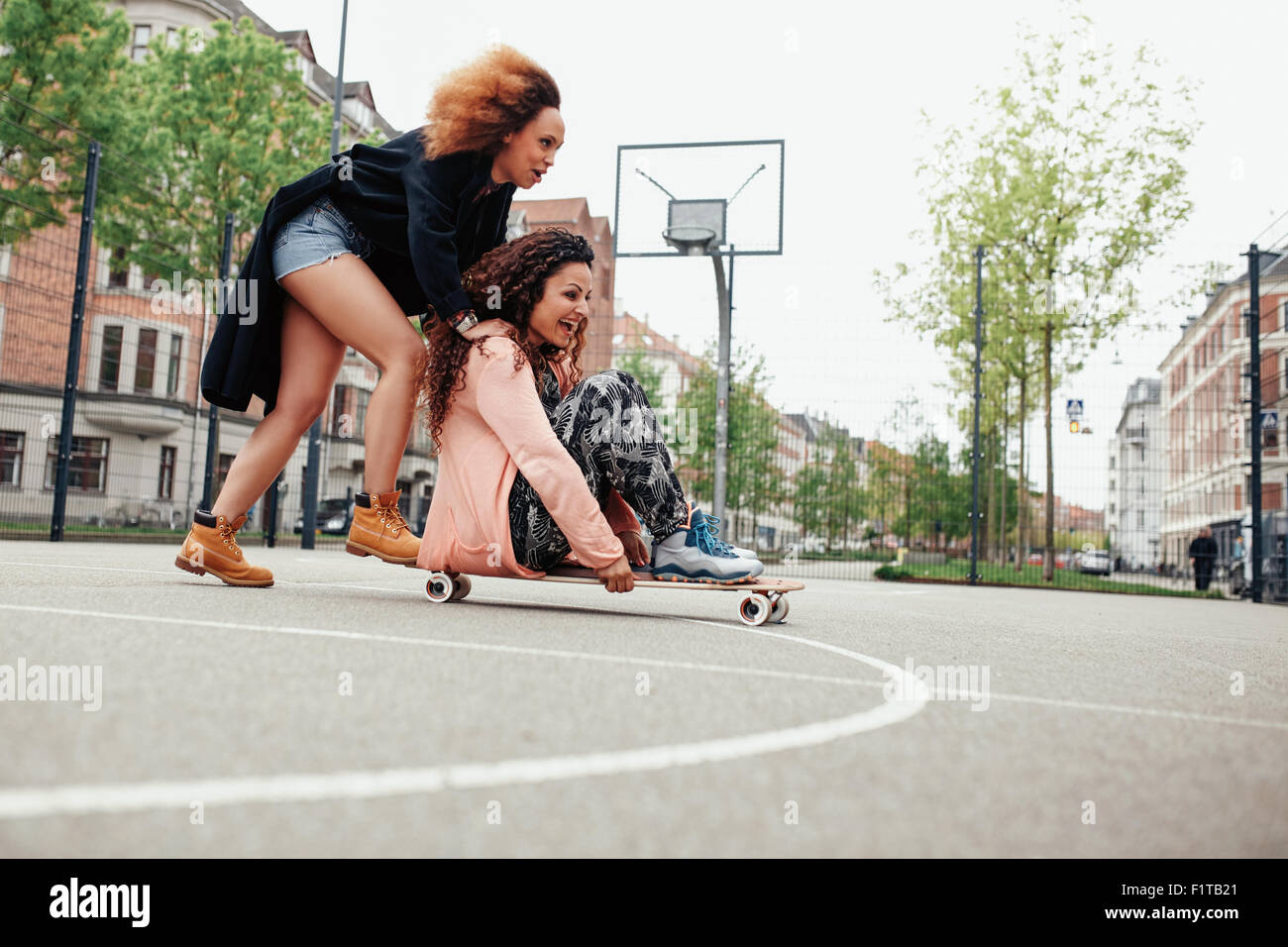 Mujer empujando a su amigo en monopatín. Las mujeres jóvenes la posibilidad de divertirse juntos al aire libre. Foto de stock