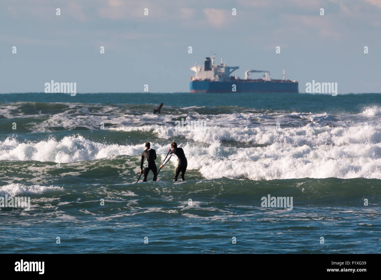 Los hombres paddleboarding on board en las olas, buque de aprovisionamiento en segundo plano. Foto de stock
