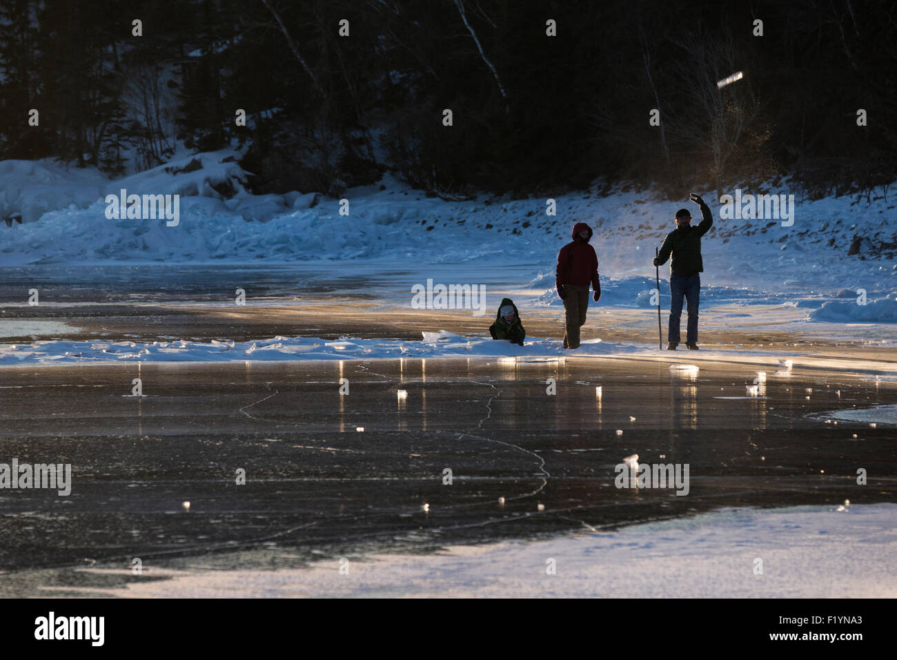 Silueta retroiluminado de hombre, mujer y niño familia afuera lanzando trozos de hielo en el aire sobre el lago congelado Superior i Foto de stock