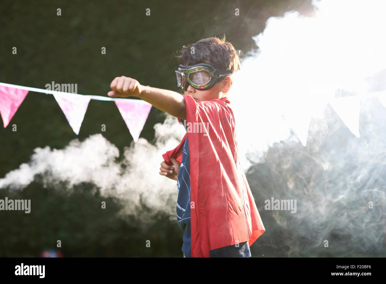 Chico gafas protectoras y cabo en superhéroe postura frente de nube de humo Foto de stock