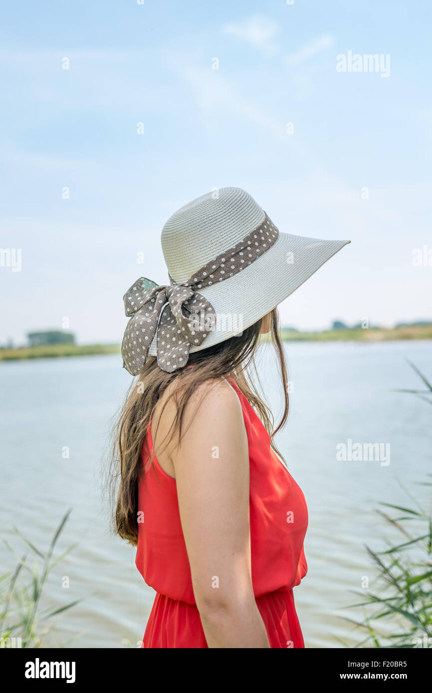 Mujer joven llevar sombrero y vestido rojo, mirando al horizonte Foto de stock