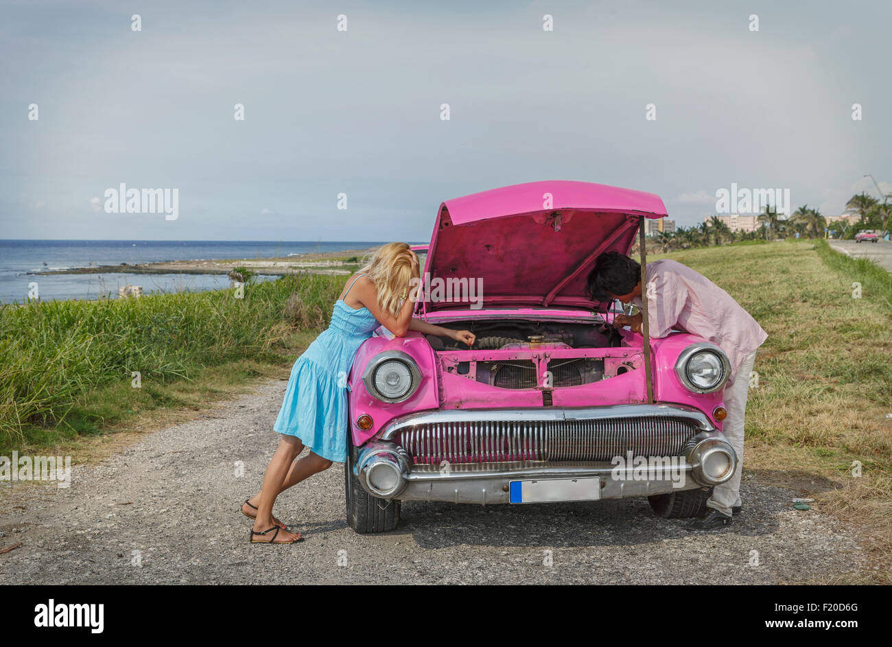 Pareja joven tratando de arreglar una vendimia convertible en la costa, La Habana, Cuba Foto de stock