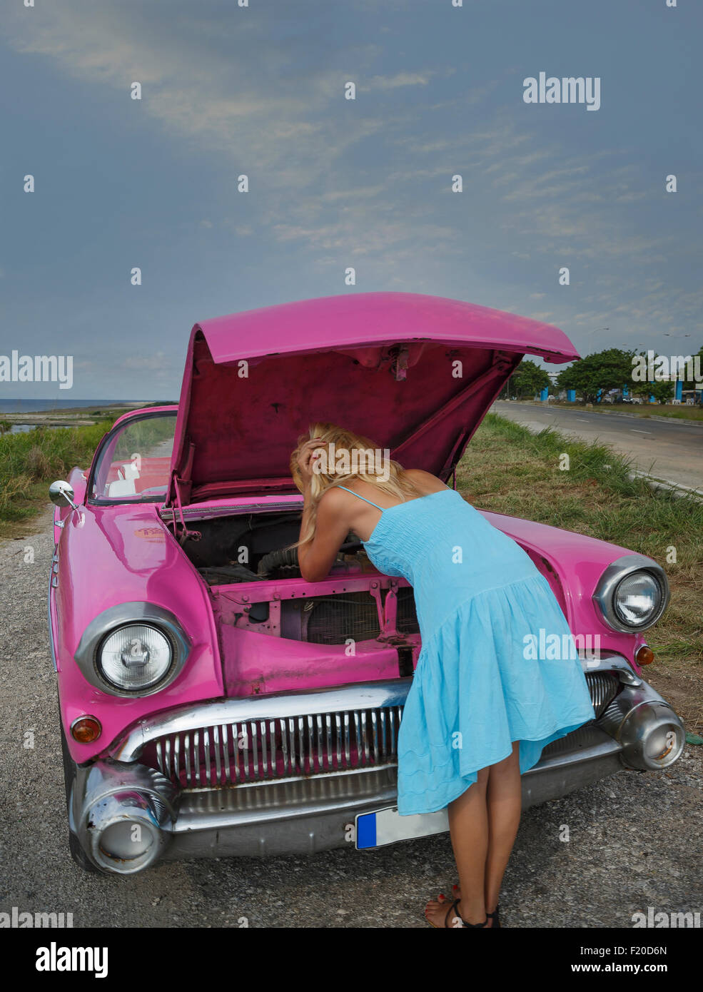 Mujer joven tratando de arreglar una vendimia convertible en la costa, La Habana, Cuba Foto de stock