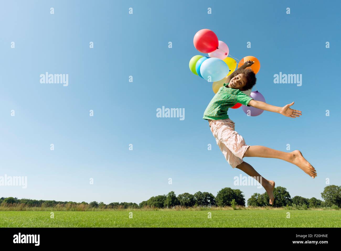 Niño sosteniendo ramo de globos saltando en el campo el aire. Foto de stock