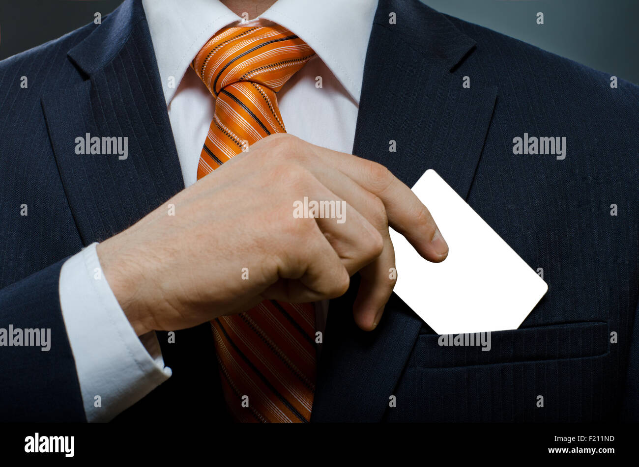 Empresario de traje negro y corbata naranja poner o sacar la tarjeta de crédito en el bolsillo Foto de stock