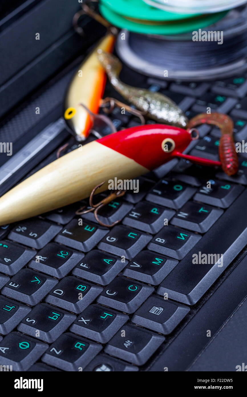 Equipo de pesca, línea de señuelo, swimbait oscuro sobre un teclado portátil. Preparar al viaje de pesca, tiendas en línea, foros Foto de stock