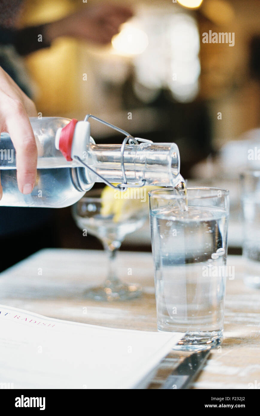 Una mano de verter agua de una botella con un clip top en un vaso. Foto de stock