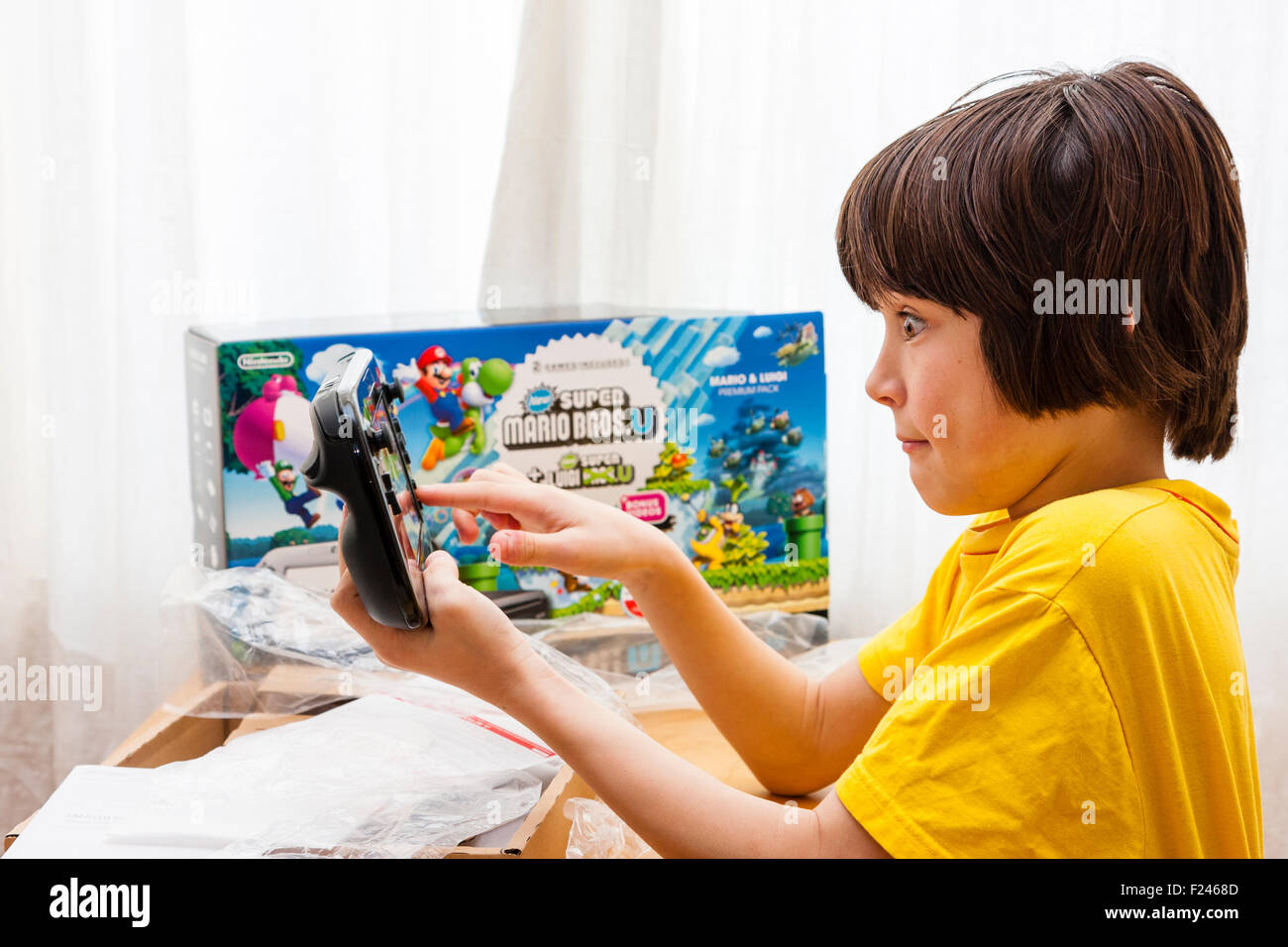 Hijo varón caucásico, muchacho, 11-13 años, sosteniendo en ambas manos una consola Nintendo Wii U justo después de sacarlo de la caja, que está junto a él. Foto de stock